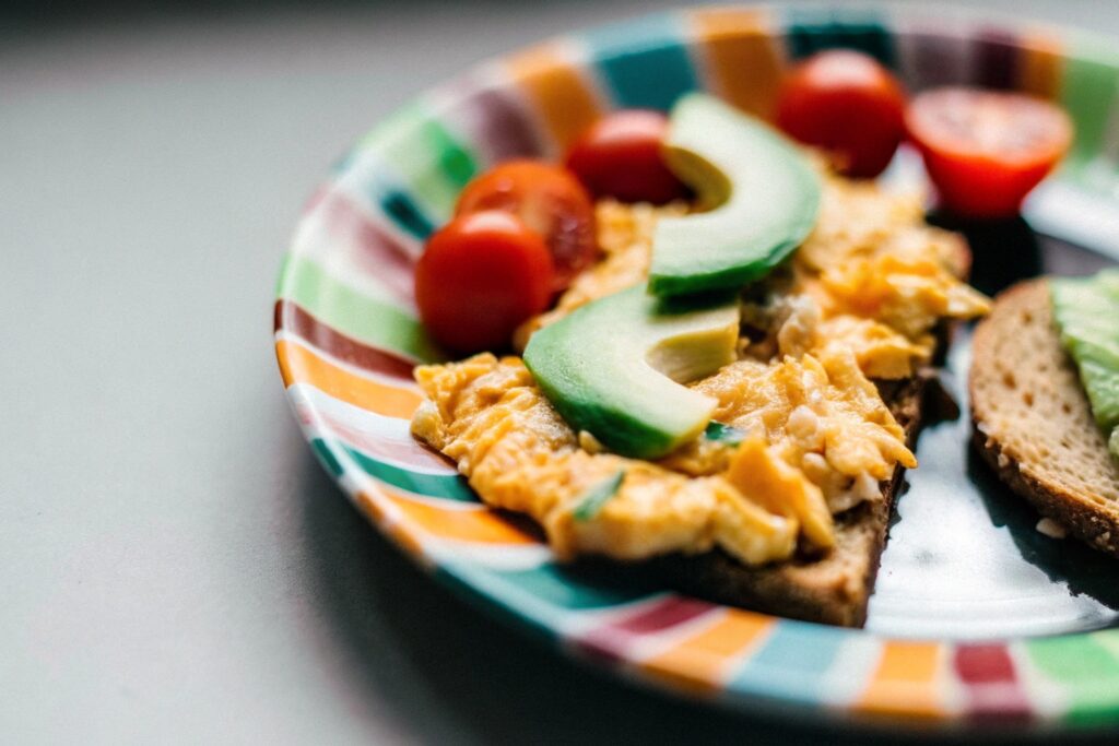 A vibrant breakfast plate showcasing scrambled eggs, creamy avocado slices, and whole-grain toast garnished with cherry tomatoes