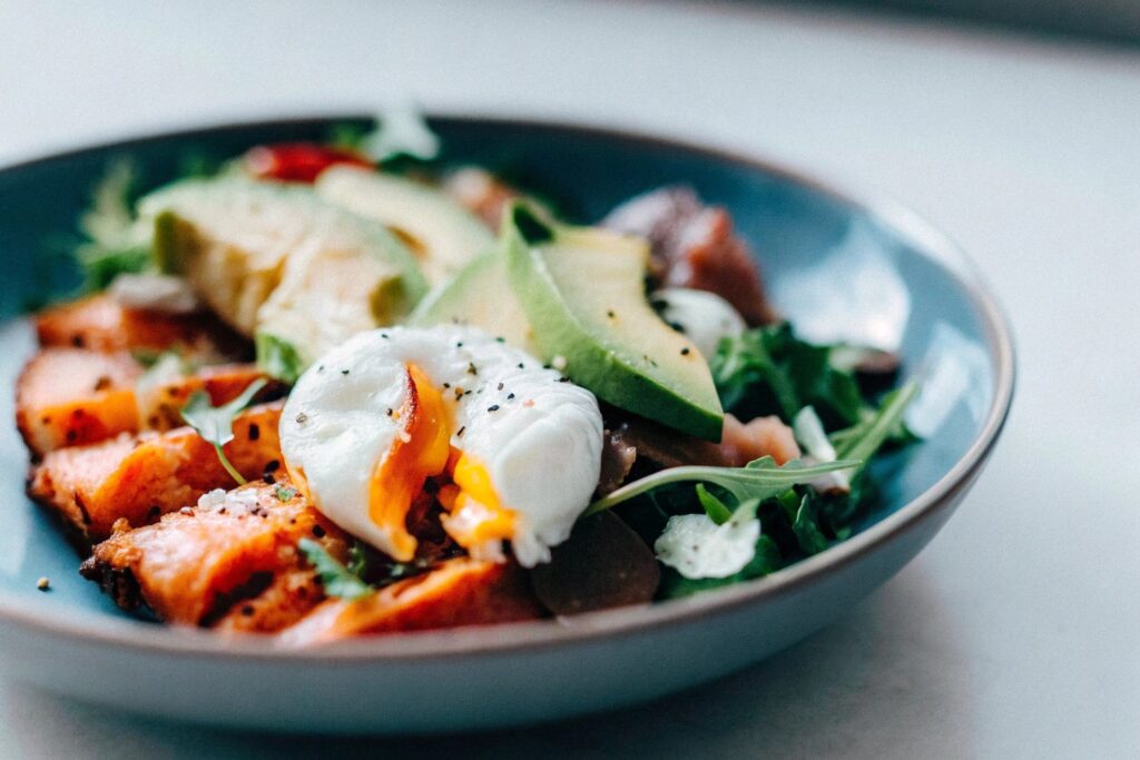 A vibrant plate featuring a salmon breakfast bowl with avocado, poached egg, and fresh greens.