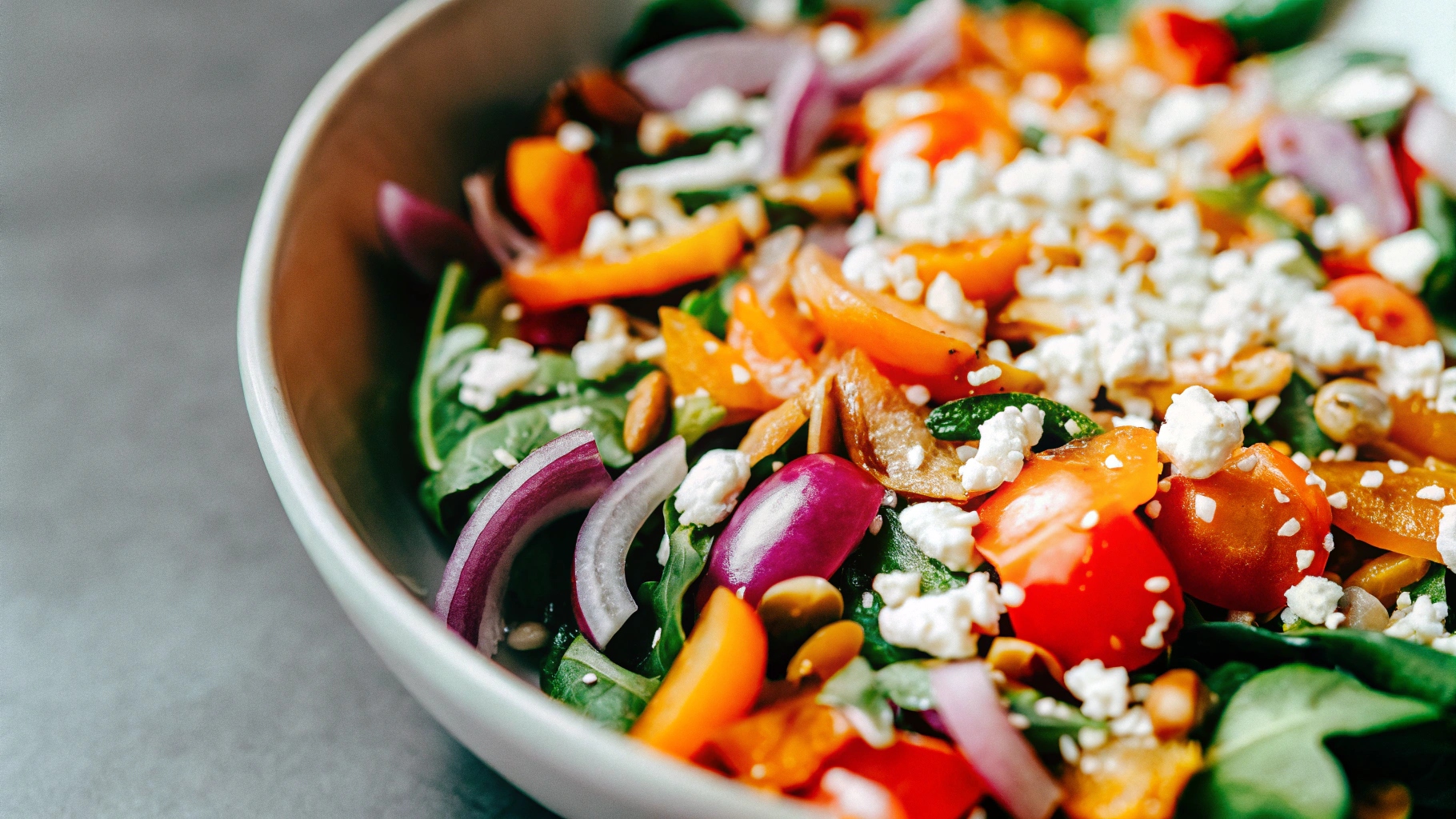 A vibrant salad with mixed greens, cherry tomatoes, red onions, pepitas, and a generous topping of cotija cheese in a white bowl