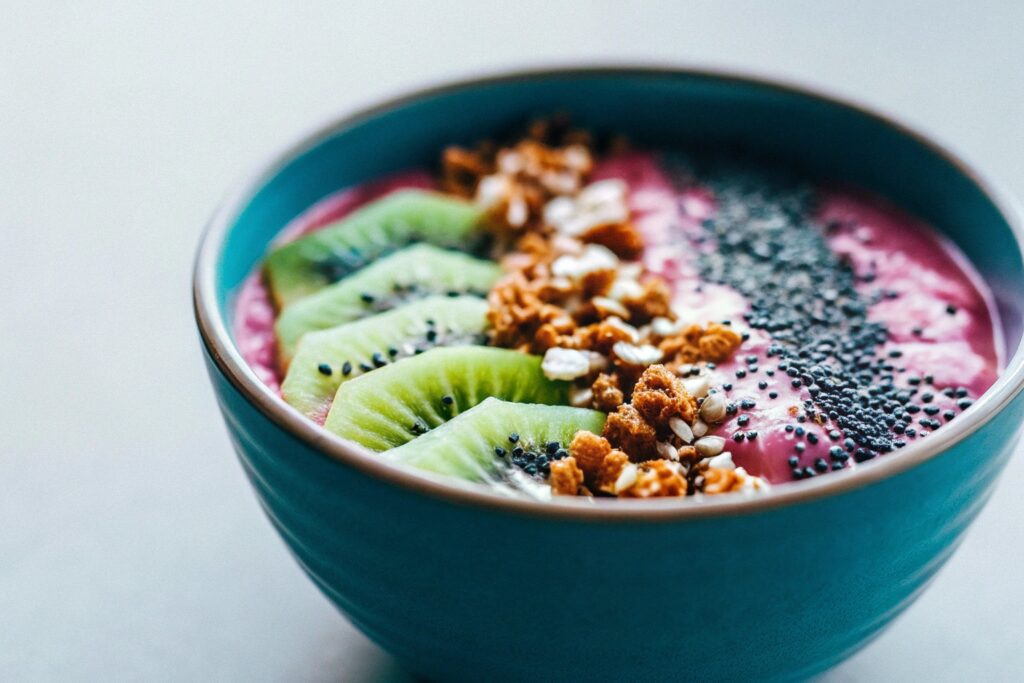 A vibrant smoothie bowl with a gradient of pink and purple, topped with kiwi slices, granola, and a sprinkle of chia seeds