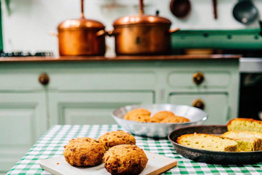 A vintage-style illustration of a French kitchen preparing croquettes, contrasted with a Southern family dinner table featuring salmon patties, cornbread, and sides