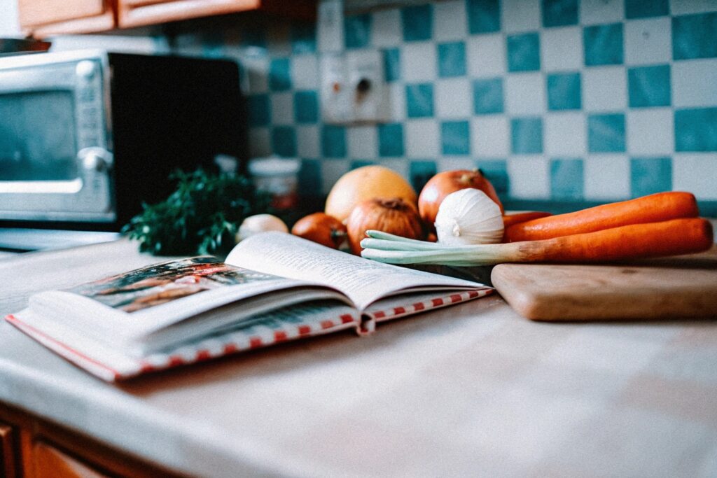 A vintage-style kitchen scene with a cookbook open to a meatloaf recipe, next to a packet of Lipton onion soup mix and fresh ingredients