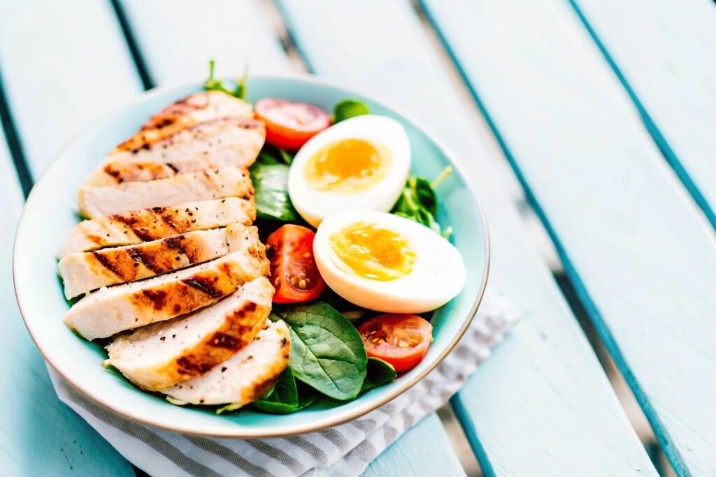 A well-balanced breakfast plate featuring sliced grilled chicken, a boiled egg, and fresh greens on a rustic wooden table