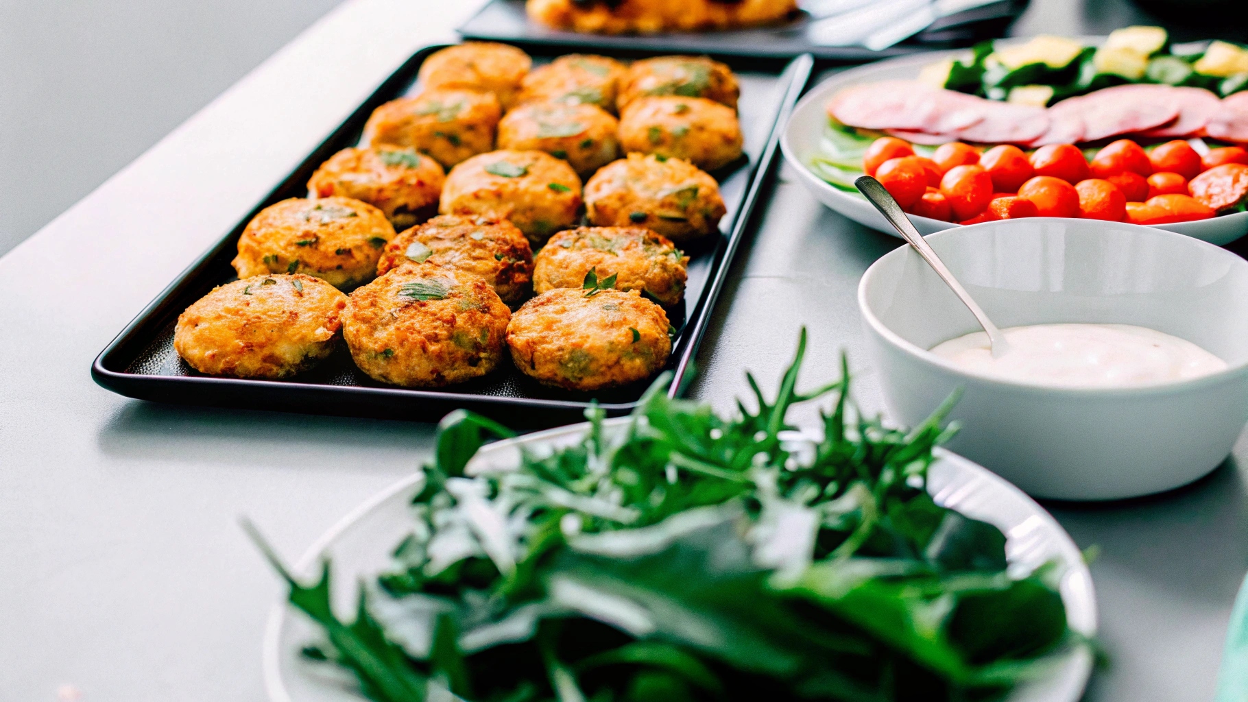 An inviting dinner table setup with a platter of golden salmon patties on one side and a plate of crisp salmon croquettes on the other, surrounded by fresh garnishes and dipping sauces