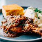 A cozy dining table with a serving dish of chicken and gravy, paired with mashed potatoes and cornbread, ready to be enjoyed.