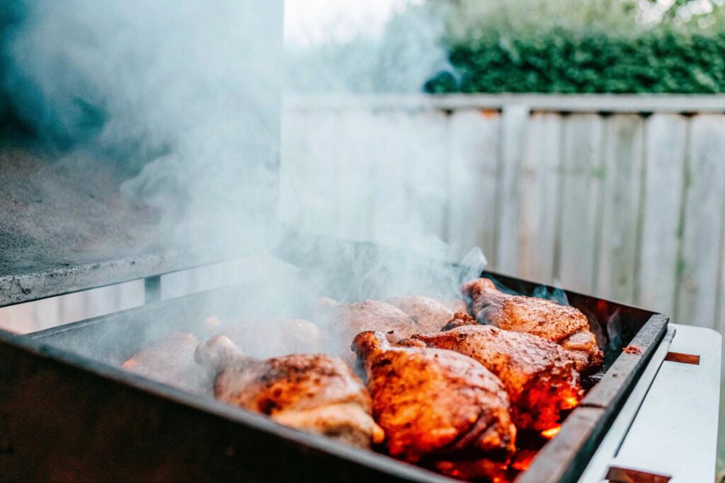 Chicken thighs smoking on a grill with wisps of smoke rising and wood chips glowing below