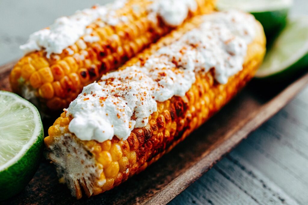 Freshly grilled corn on the cob coated with mayonnaise, chili powder, and crumbled cotija cheese, served on a rustic platter with lime wedges