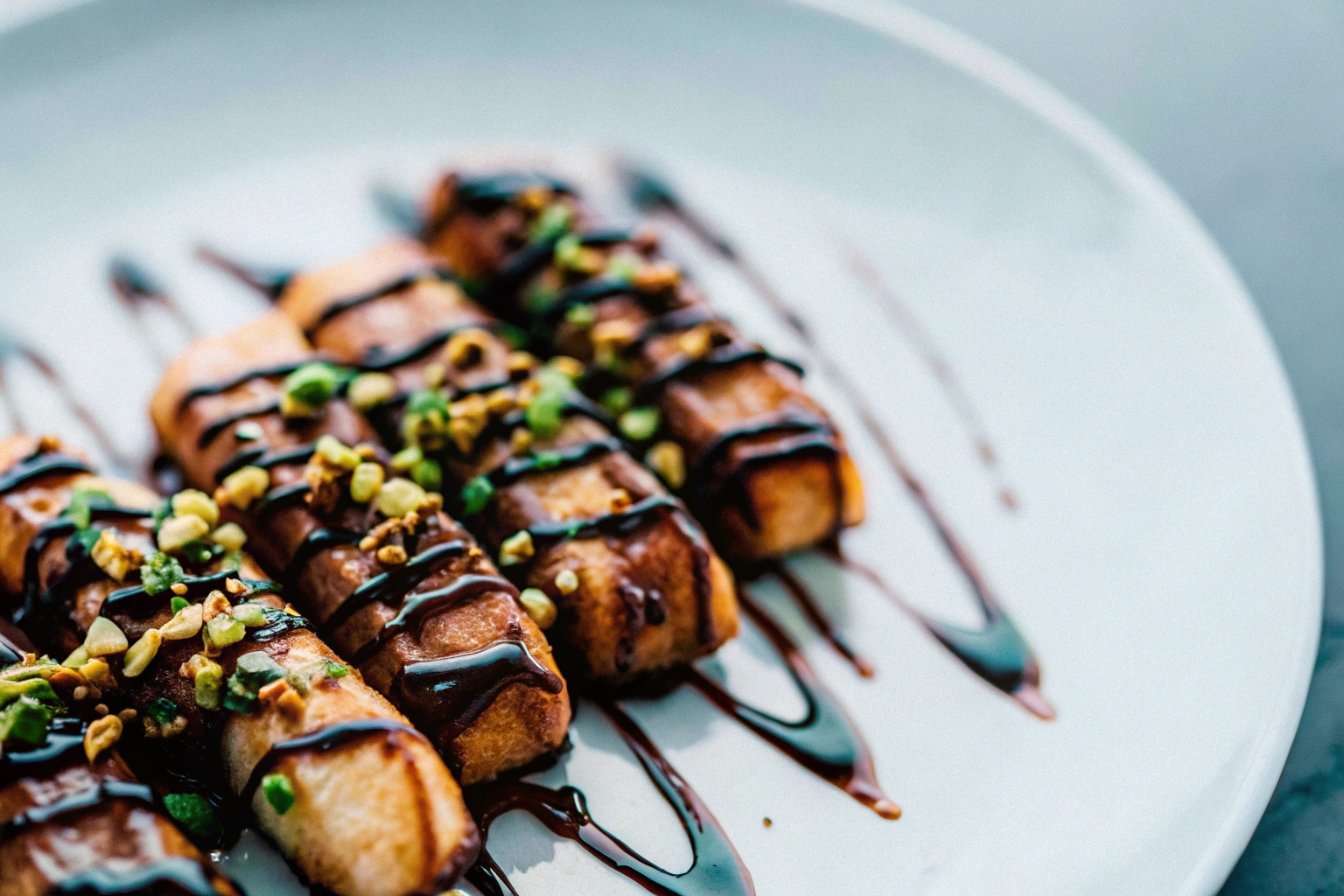 Fried bananas elegantly plated with a drizzle of melted dark chocolate and topped with crushed pistachios