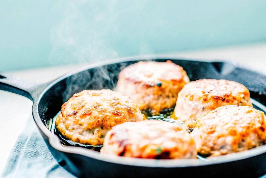 Golden-brown salmon patties sizzling in a cast-iron skillet, with a crispy crust forming as they cook.