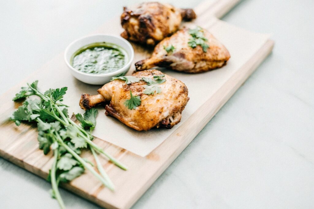 Golden-brown smoked chicken thighs on a wooden cutting board, garnished with fresh herbs and accompanied by a side of dipping sauce