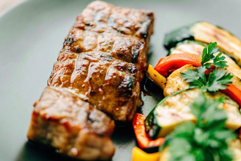 Grilled boneless short ribs coated in a smoky glaze, served alongside charred vegetables and garnished with fresh parsley on a wooden cutting board