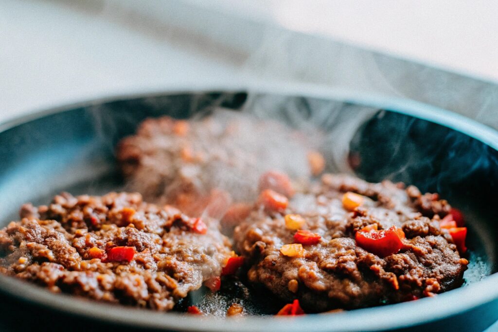 Ground beef cooking in a hot skillet, seasoned with spices like chipotle chili powder and cumin, with visible steam rising