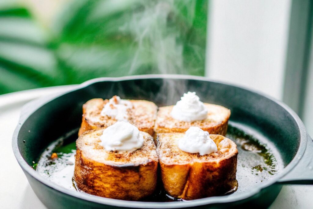 Hawaiian Roll French Toast cooking on a nonstick skillet, golden-brown with melted butter sizzling around the edges.