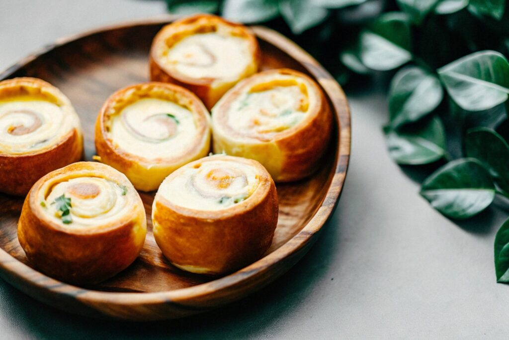 Hawaiian rolls dipped in a rich custard mixture, placed on a rustic wooden plate with a warm, textured background.