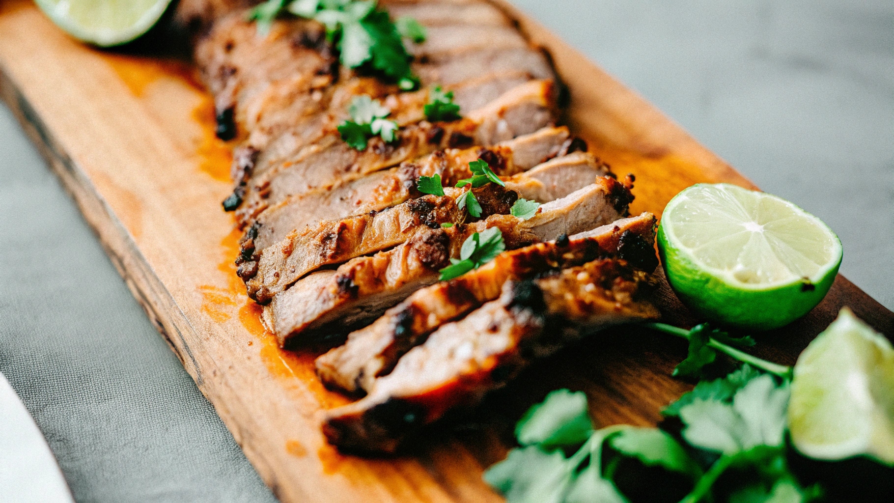 A plated chipotle steak served with grilled corn on the cob, a side of rice, and lime wedges on a rustic wooden table