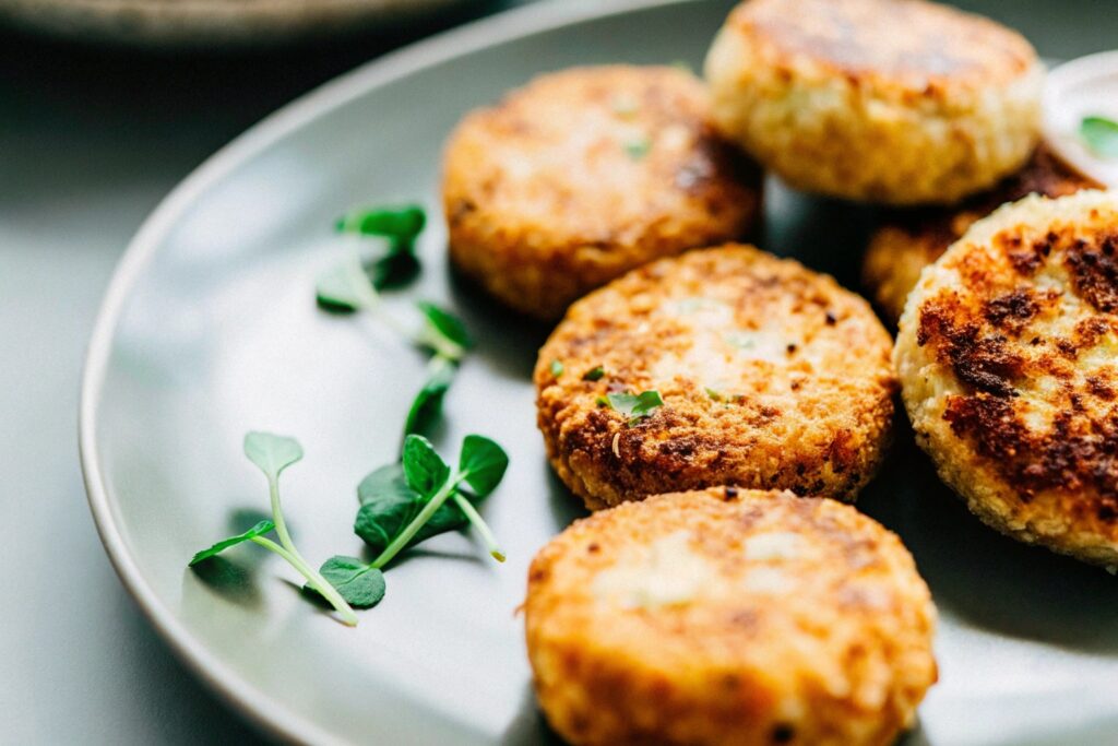 A rustic kitchen counter displaying two plates: one featuring golden salmon patties and the other showcasing crispy salmon croquettes, garnished with fresh herbs