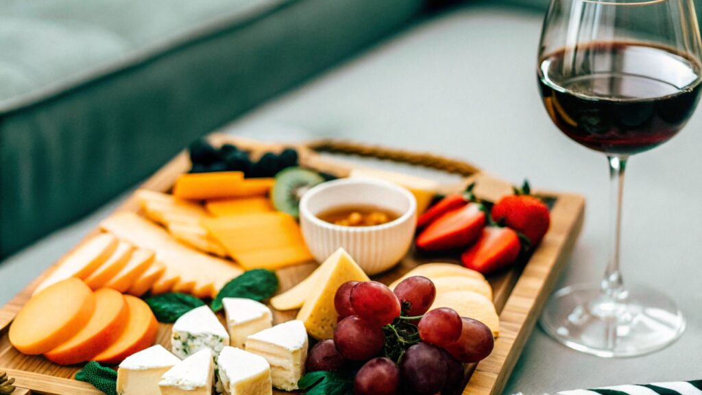 A beautifully arranged cheese board featuring Brie cheese bites, fresh fruits, and wine glasses, styled for an elegant gathering