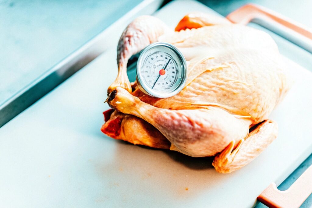 Raw chicken pieces on a wooden cutting board with a meat thermometer, demonstrating safe cooking preparation