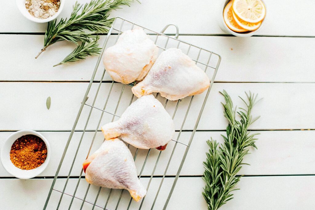 Raw chicken thighs arranged on a wire rack with seasoning ingredients displayed around them on a rustic wooden surface