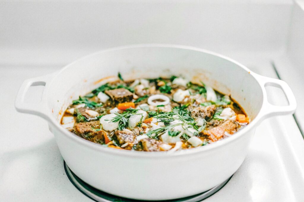 Short ribs cooking in a cast-iron pot with onions, carrots, and a red wine reduction gently simmering