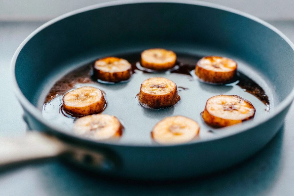 Slices of bananas frying in a non-stick skillet with a light drizzle of coconut oil and a golden-brown crust forming