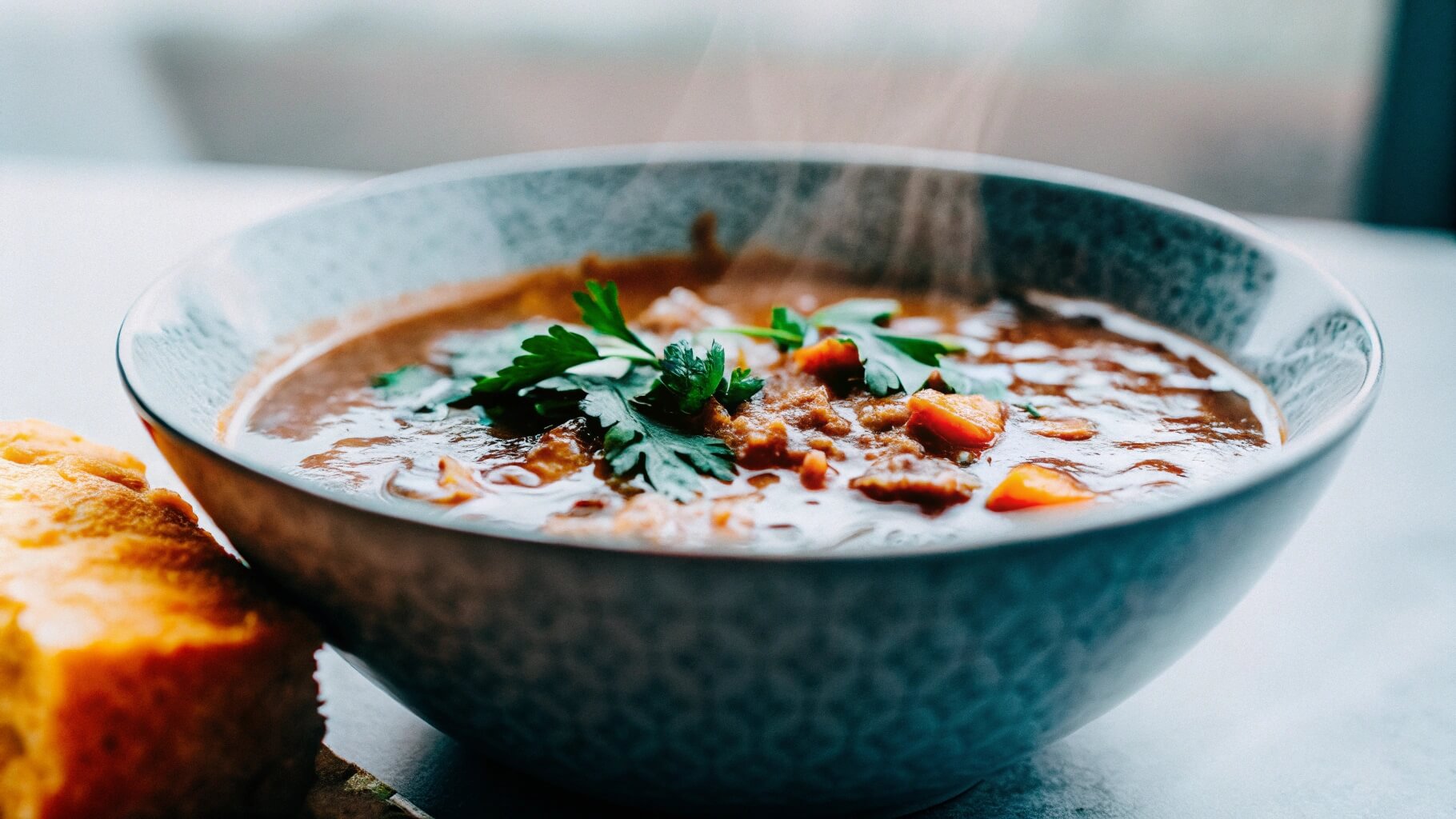 A bowl of swamp soup served with a side of cornbread, garnished with fresh parsley, with steam rising from the bowl